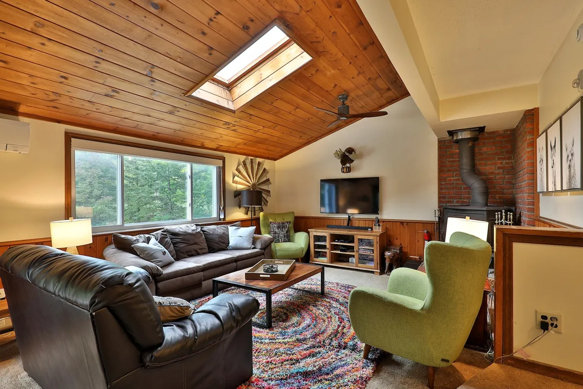 A warm and welcoming living room featuring a comfortable sofa, cozy rug, skylight letting in natural light, TV, and a centerpiece fireplace. The inviting layout encourages both relaxation and social gatherings, perfect for unwinding after a day on the slopes.