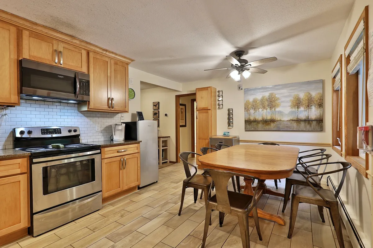 This image showcases a warm and welcoming dining area with wooden cabinetry, stainless steel appliances, and a dining table set up for group meals. The space exudes an inviting atmosphere ideal for family gatherings, celebrations, and shared experiences.