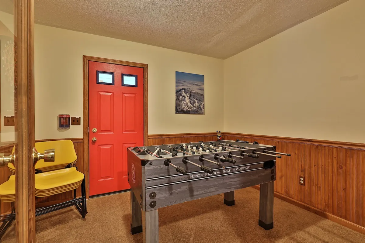A bright and playful game room centered around a foosball table, with a vibrant red door and yellow chairs that add to the fun atmosphere. The space is designed for friendly competition and group enjoyment.