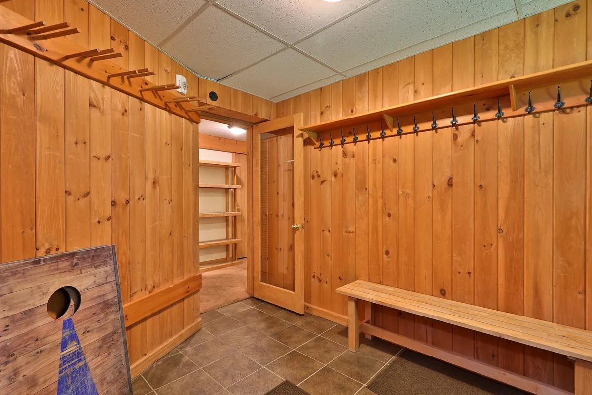 A functional mudroom with wooden wall panels, robust hooks for outerwear, a bench for sitting or removing shoes, and an open door leading to the rest of the home. The space is cozy yet utilitarian, designed for organizing gear and providing a transition from outdoor adventure to indoor relaxation.