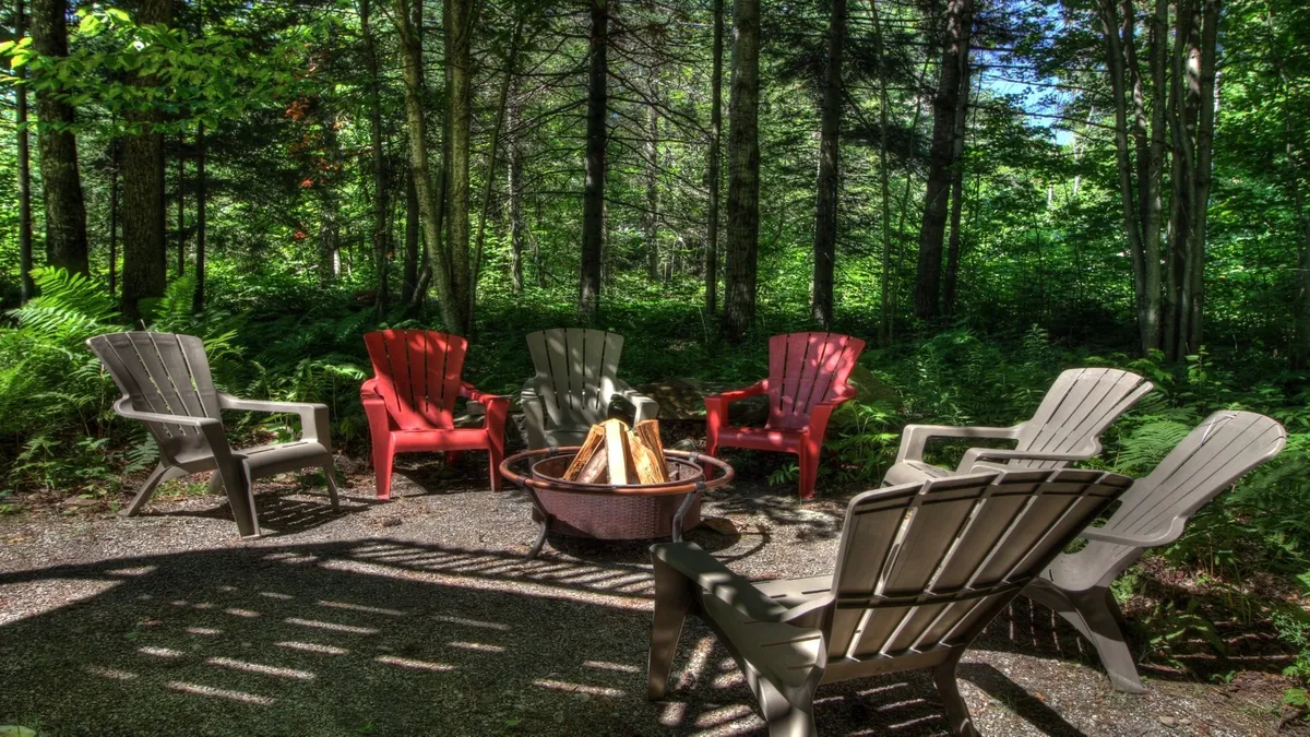 A cozy outdoor fire pit surrounded by Adirondack chairs nestled among trees. The scene exudes a communal, relaxed atmosphere perfect for evening gatherings and storytelling.