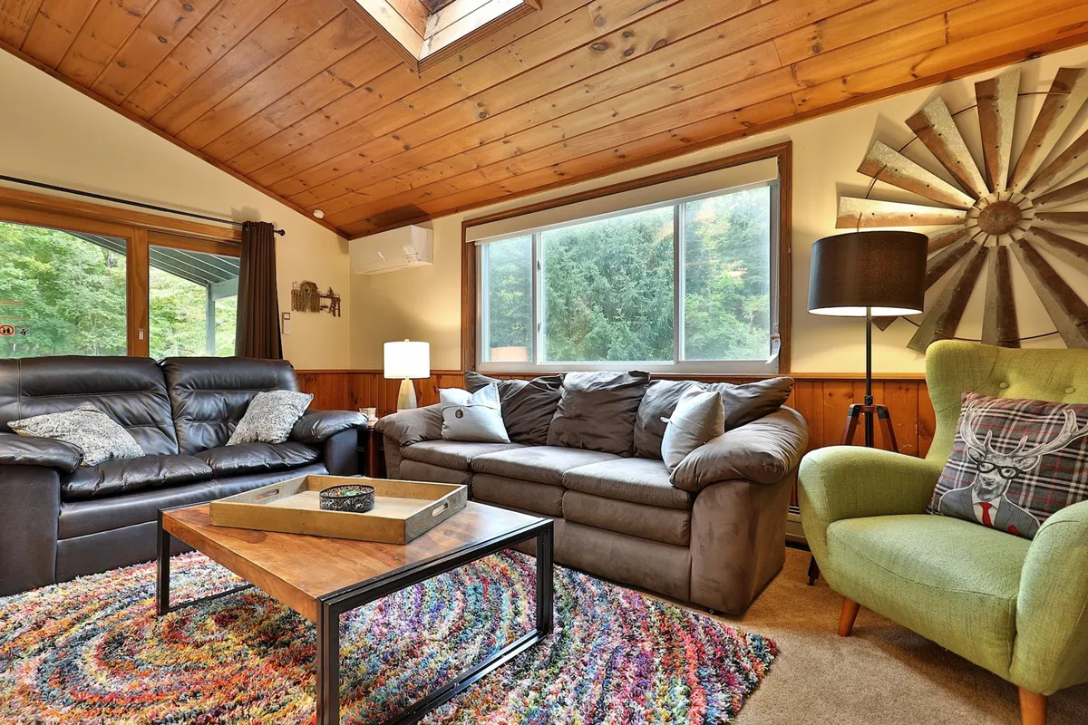 A comfortable living room with leather sofas, a colorful area rug, a wooden coffee table, a green armchair, and a large window. The room is ideal for relaxing, playing games, or gathering for movie nights, as described in the section.